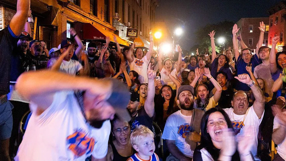 Dozens of fans cheering and watching a basketball game in the street