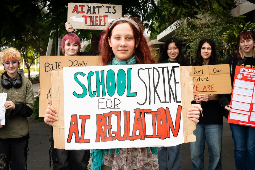 Young woman holding hand painted sign reading "school strike for AI regulation" more students and signs behind her
