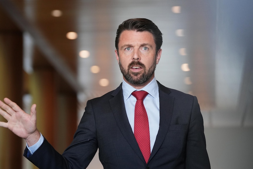 Duniam raises his right hand as he speaks from a corridor