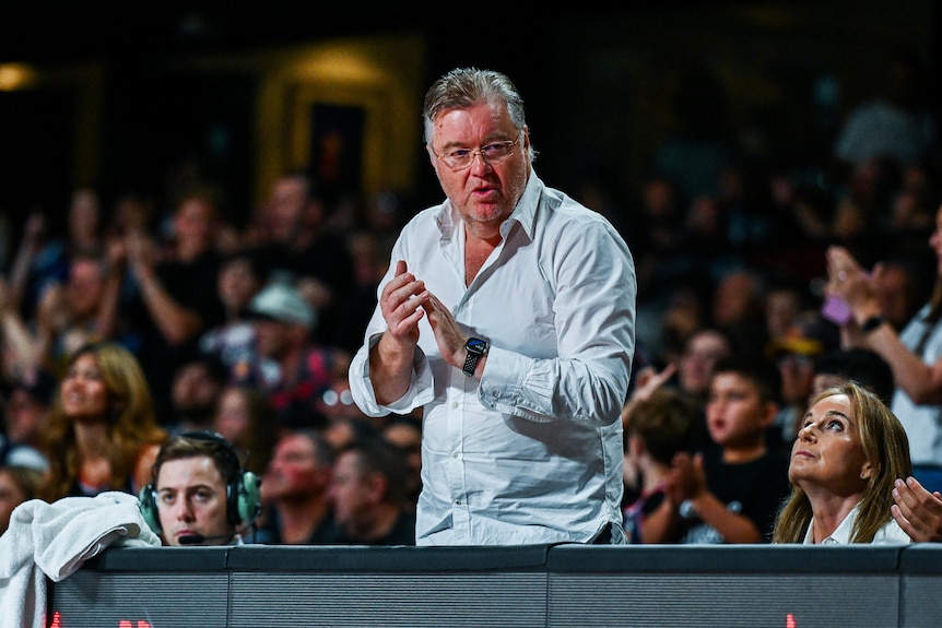 A man claps his team on from the sidelines of a basketball court.