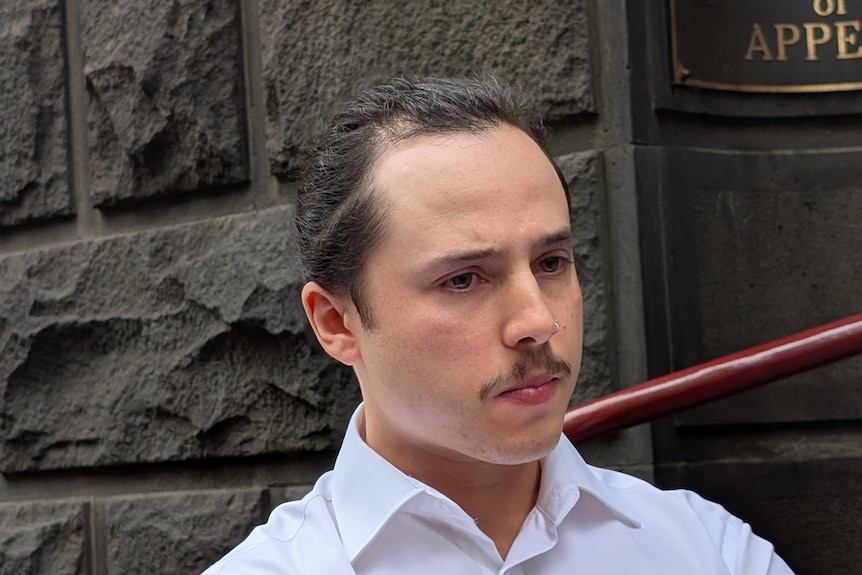 A man in white with dark hair and a ponytail