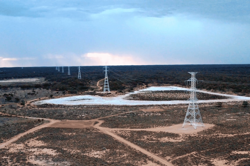 Transmission towers in a line over a vast area of desert and bushland, as seen from above.