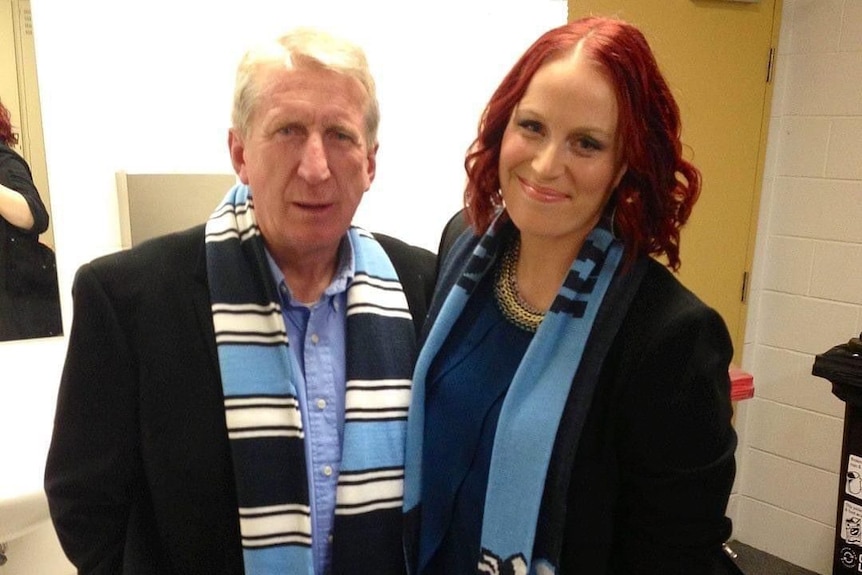 Erin with her dad as an adult in nice clothes and a footy scarf, smiling and standing next to each other.