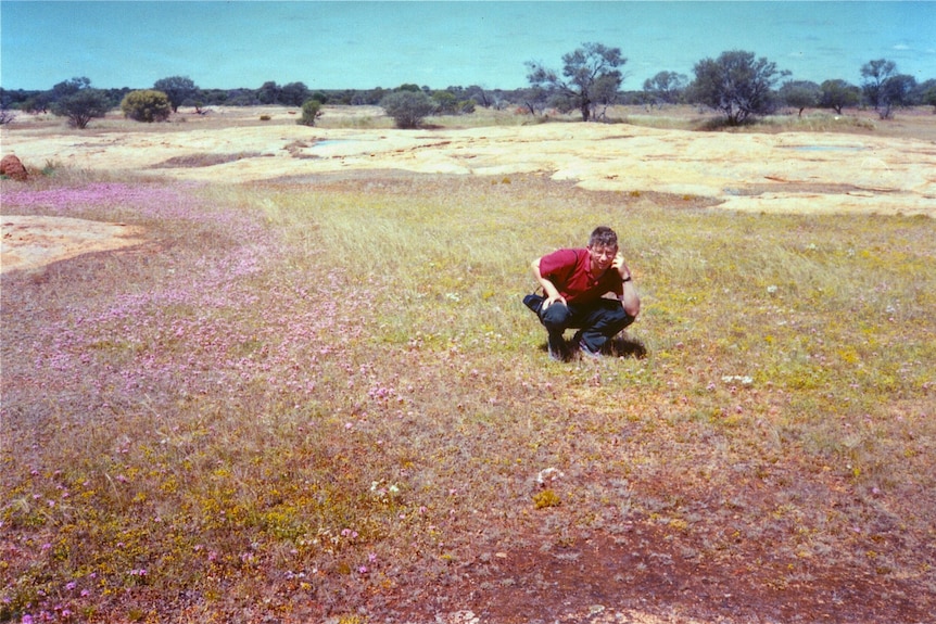 Jerry Coleby-Williams squats in a dry field with small purple flowers