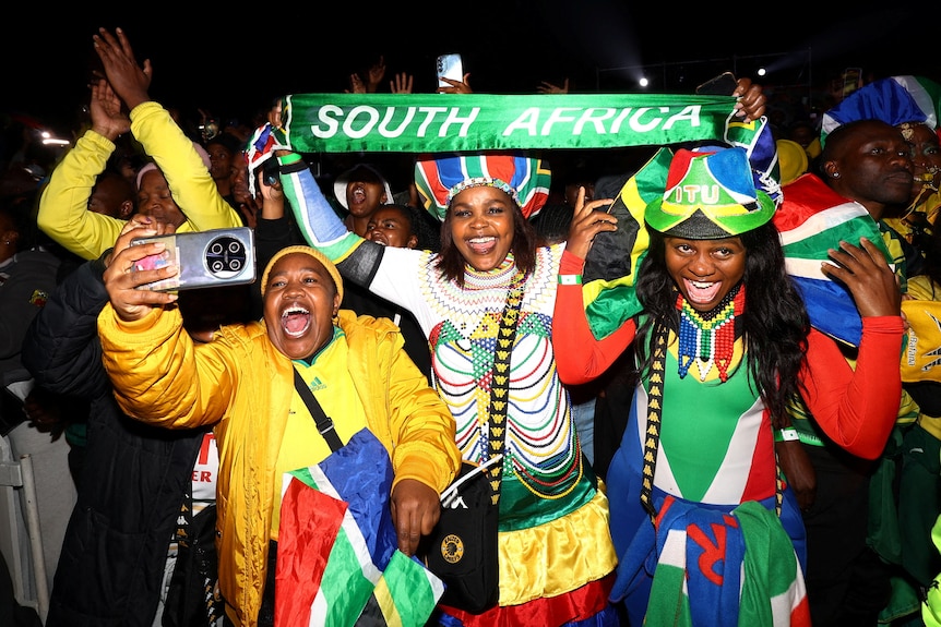 three women among a crowd dressed in the colours of the south african flag cheering