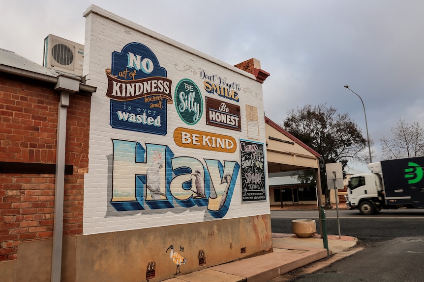 Side of a brick heritage building with a painted mural reading 'Hay' 'Be Kind' 'Be Silly' "Don't Forget to Smile' 