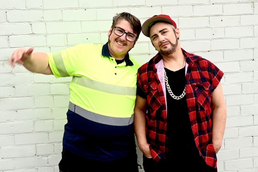 Two drag kings standing infront of a wall.