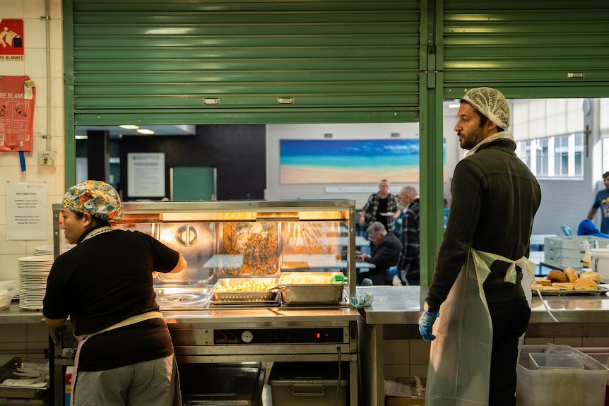 A woman and man stand in the kitchen of a hostel for homeless men.