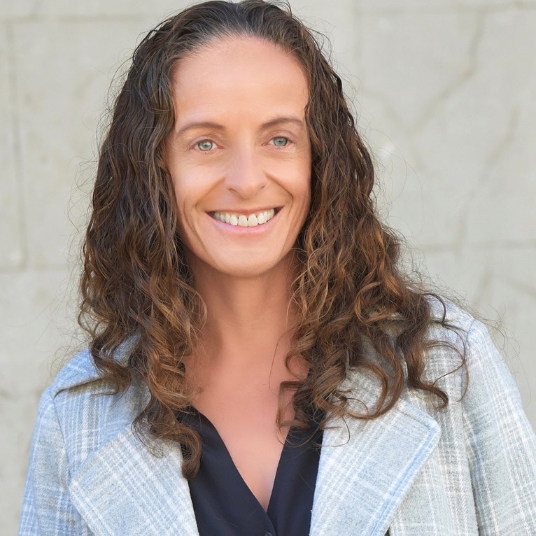 A woman with curly brown hair and a jacket smiling for the camera