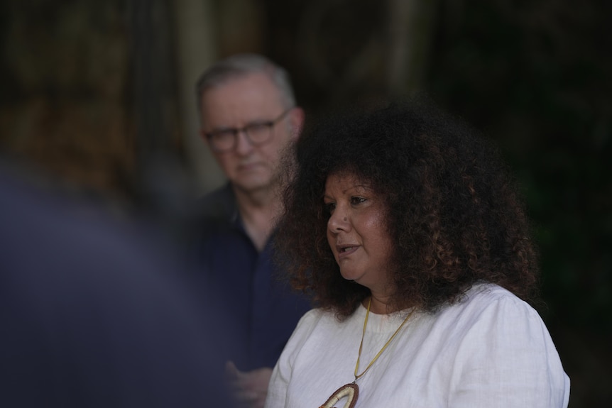 Minister McCarthy is wearing a white blouse. Prime minister Anthony Albanese is standing in the background behind her
