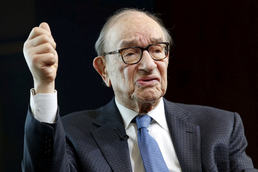 Alan Greenspan wearing a blue tie while holding his hand in a fist in the air.