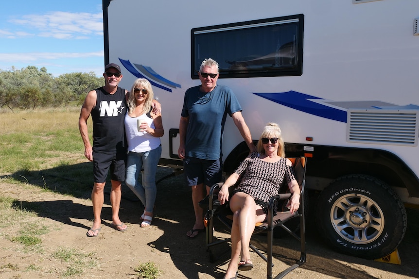 Four travellers smile outside a caravan.