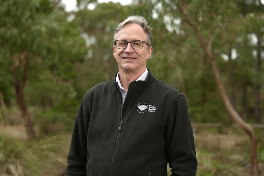 A man wearing a black jacket and glasses poses for a portait.