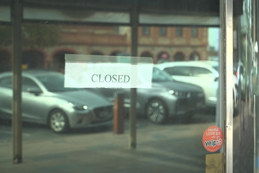 A closed sign on a glass window reflecting parked cars on the side of a street