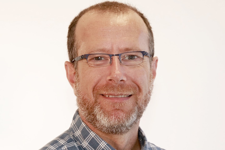 man with beard and glasses in checked shirt smiling at camera