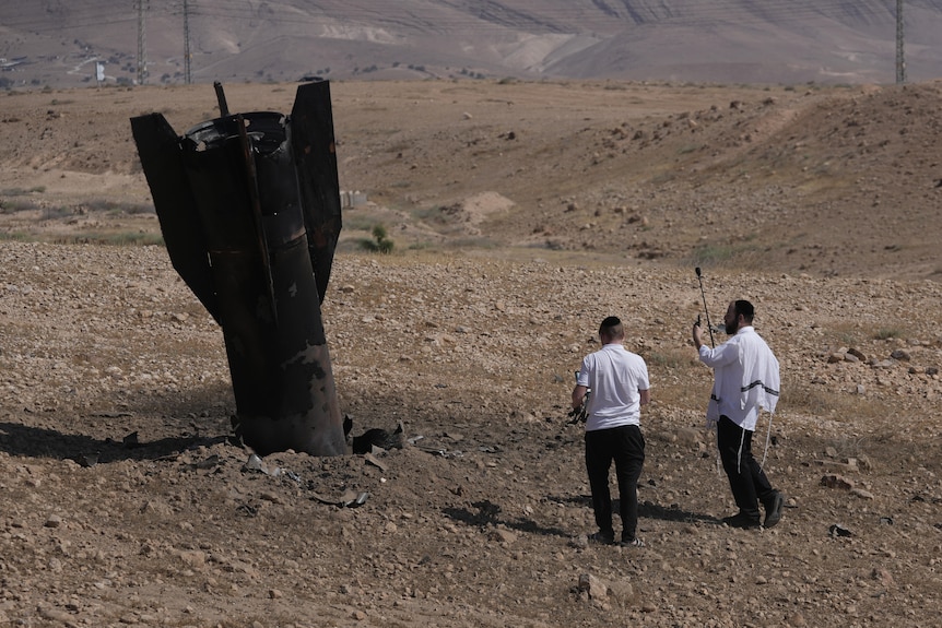 Two men look at a missile lodged into the earth 