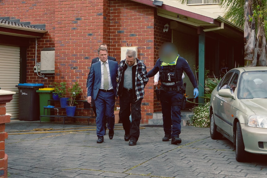 A man being arrested and walked away from a property by police. 