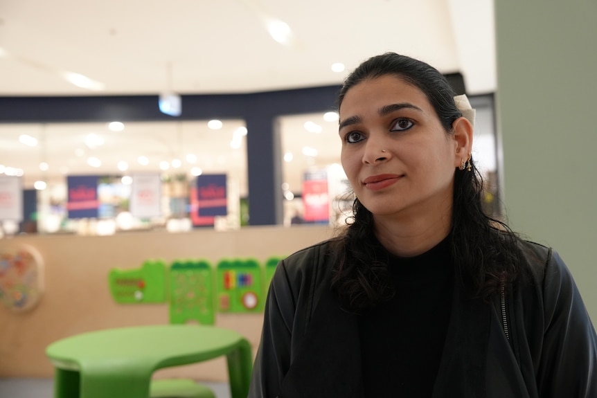 A woman with long, dark hair sits at a table in a shopping complex.