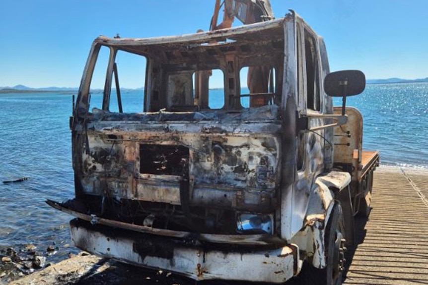 A burnt out truck at a boat ramp.