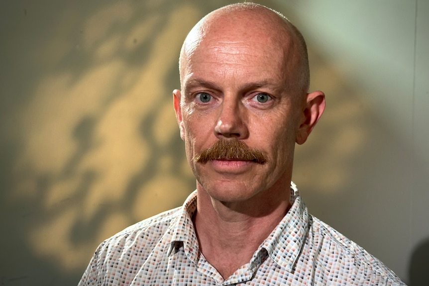 a bald man with a moustache wearing a collared shirt