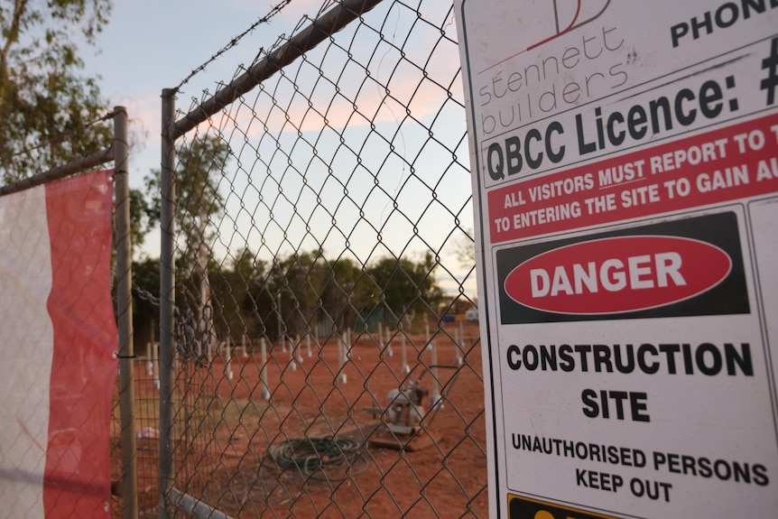 A construction warning sign hangs on a fence outside of a building site