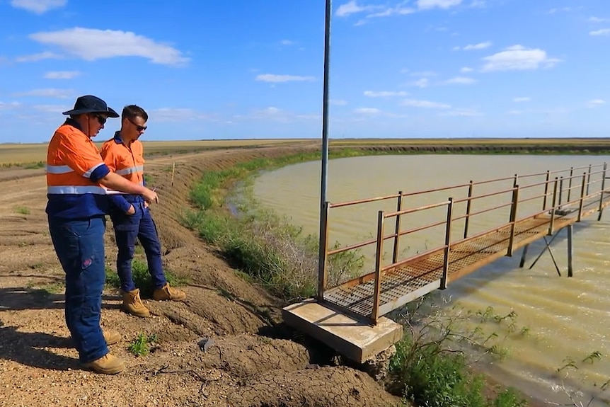 Two men in high vis stand next to a large dam with a pier.