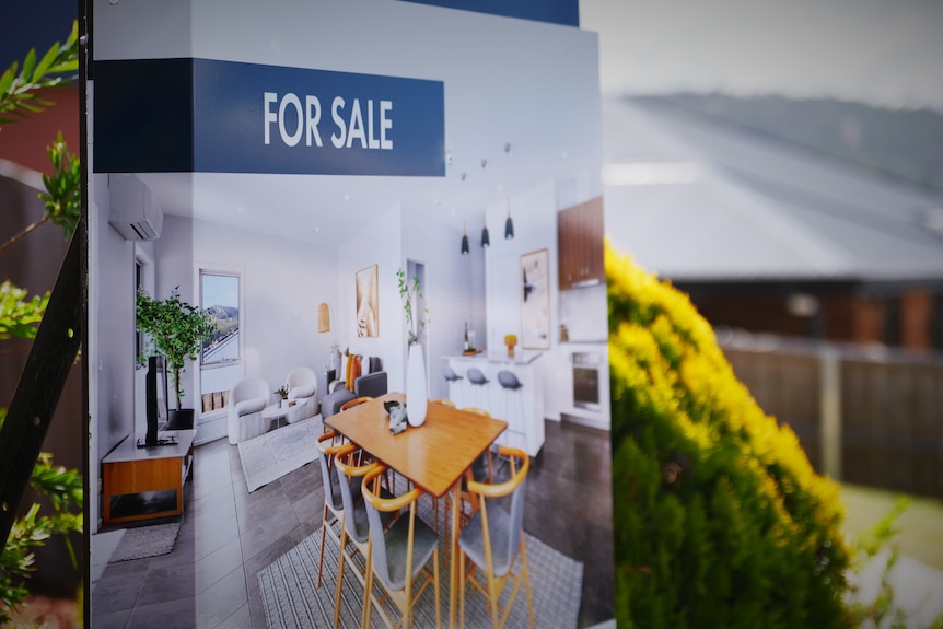 A 'for sale' sign in front of a suburban house.