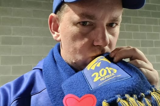 A man in a blue cap kisses a sports scarf