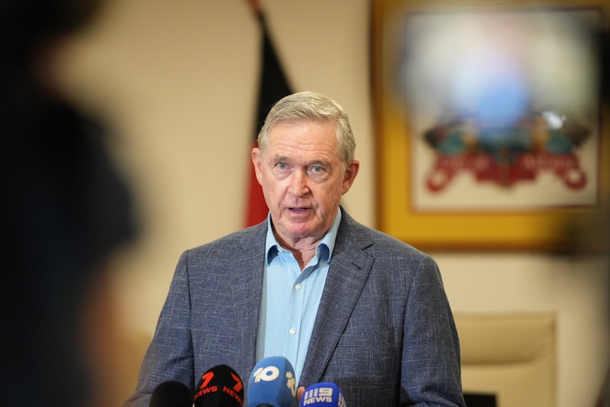 Man wearing suit jacket talking in front of microphones.