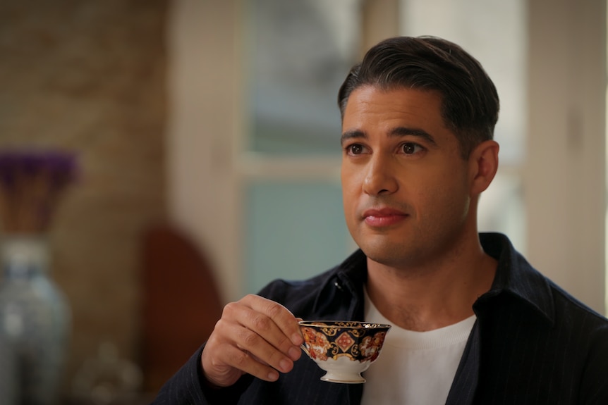 Marc Fennell holds a delicate teacup as he listens intently to someone off screen.
