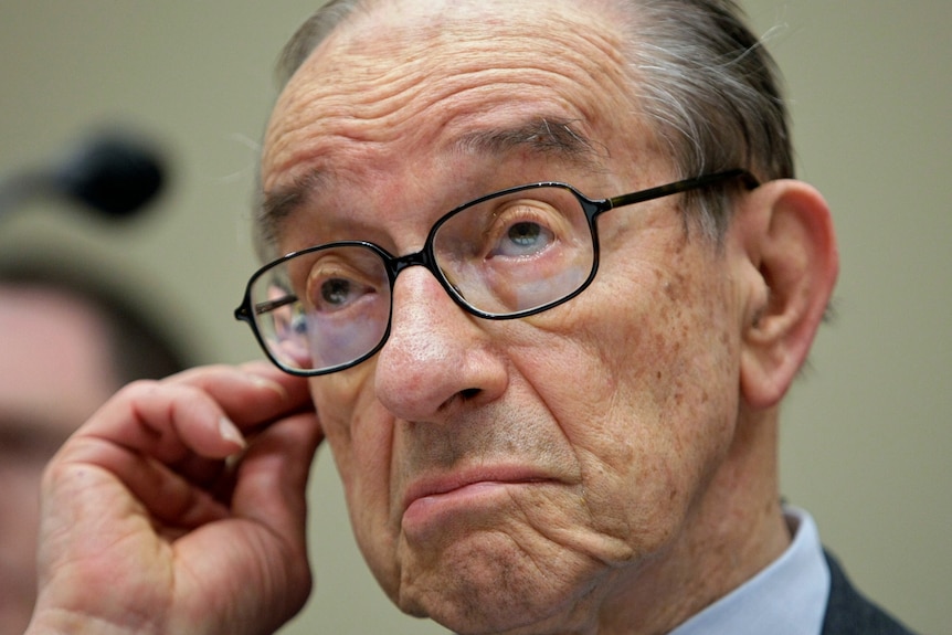A close up of Alan Greenspan with his left hand holding onto his ear.
