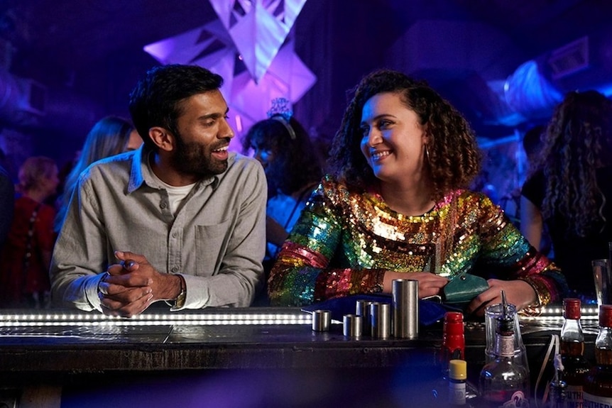 A man and a woman in a bar, both smiling and looking at each other with mutual attraction.