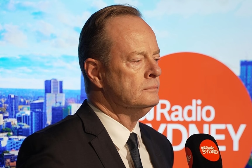 Mr Cotter in a suit with ABC Radio Sydney signage in the background speaking into a microphone.