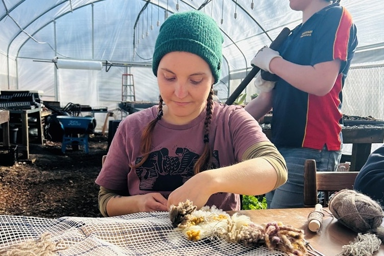 A woman in a grow tunnel making a piece of art with wool.