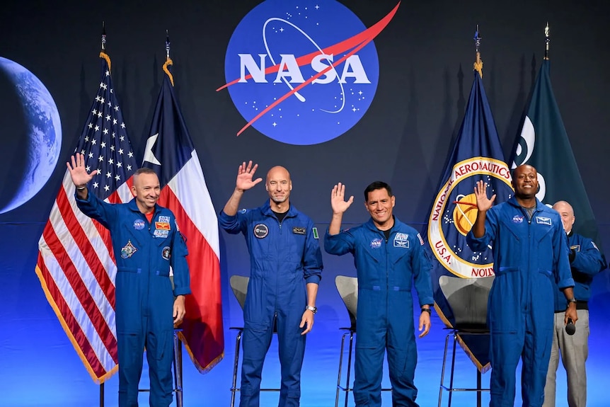 Four men in NASA uniforms wave to a crowd.