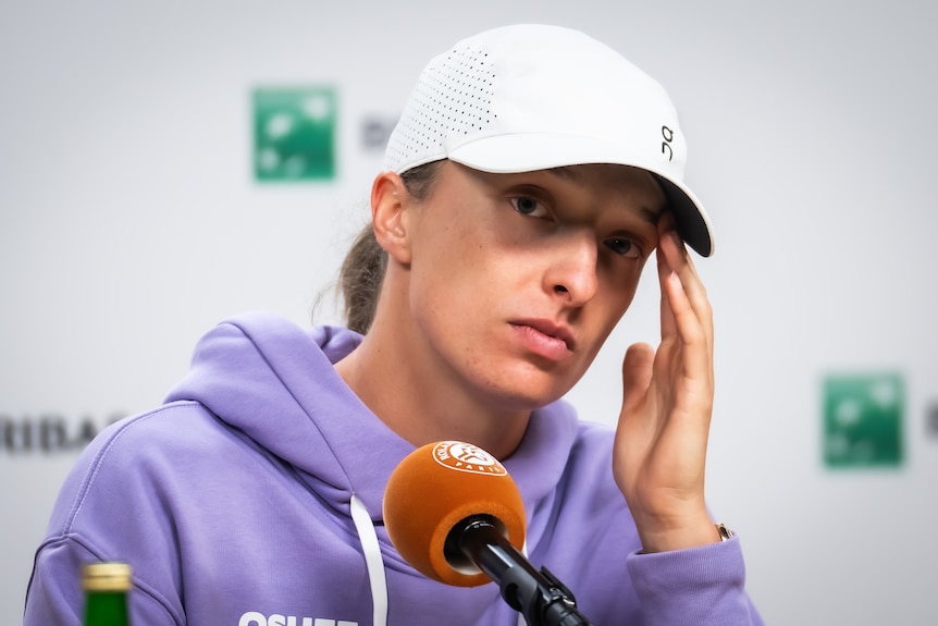 Iga Swiatek touches her head while looking glum in a French Open press conference.