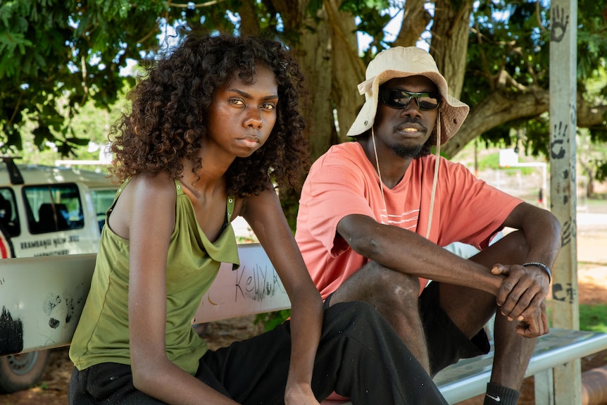 Two young Aboriginal actors, a woman and a man, looking at the camera while sitting on a bench.