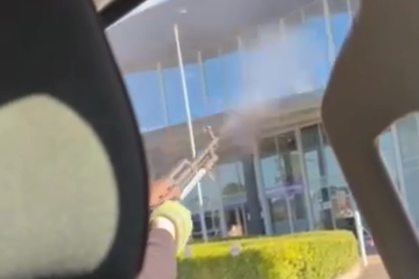 Semi-automatic rifle barrel outside an car window with smoke coming out end. Glass and dark building in background