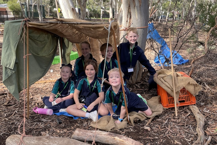 kids sit under a tarp they've fashioned into a tent in the bush