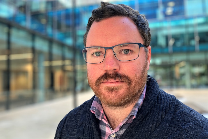 Close up of a man with a beard and glasses who looks frustrated.