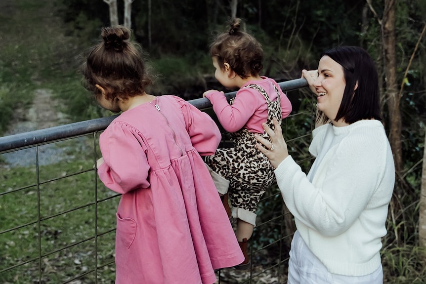 A smiling woman with two children in a rural setting.