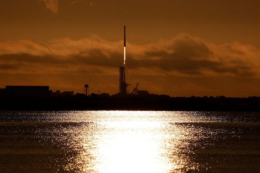 A rocket launches into the sky above a large body of water