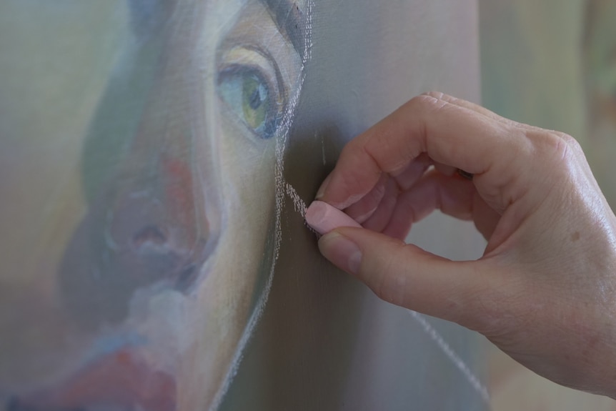 A close up of a woman's hand with chalk, drawing a portrait image.