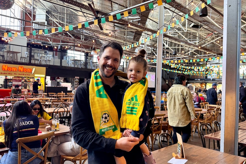 A man carries a toddler with the socceroos scarf around them inside a cafe