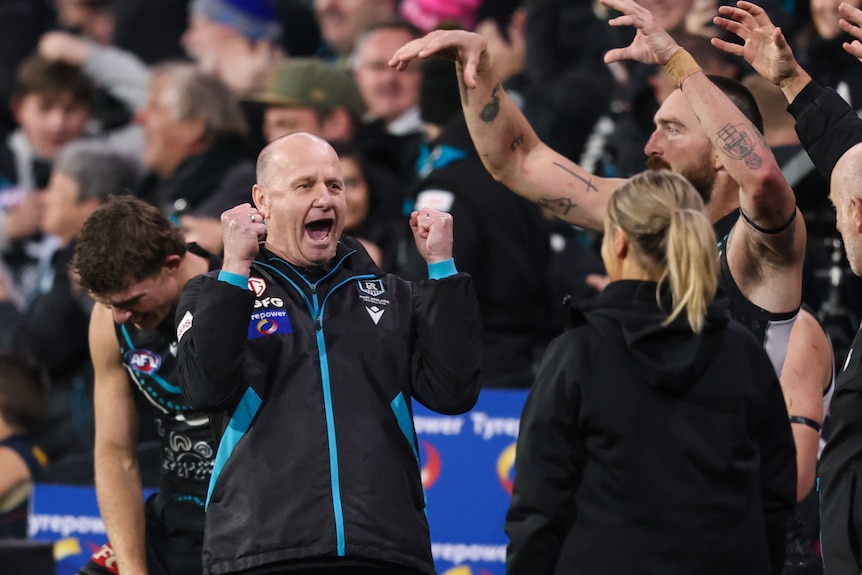 Coach celebrates with players, staff, in front of fans, at full-time of an AFL match