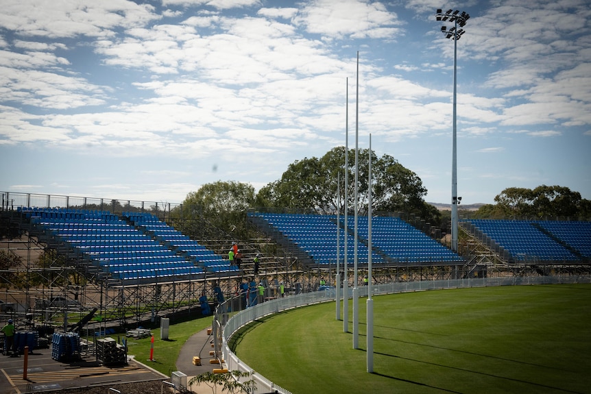 A football oval with workers putting up temporary seating and scaffolding.