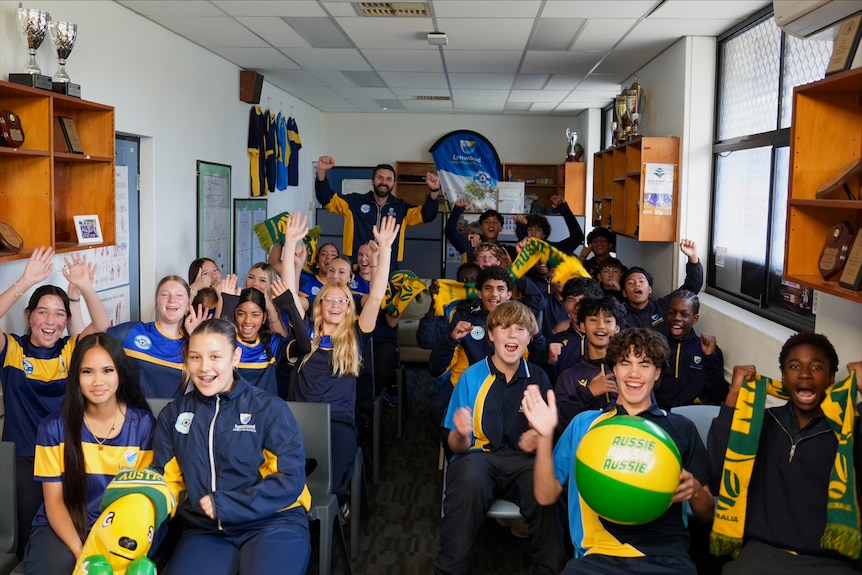 A school room full of kids sitting in chairs watching the game and smiling.