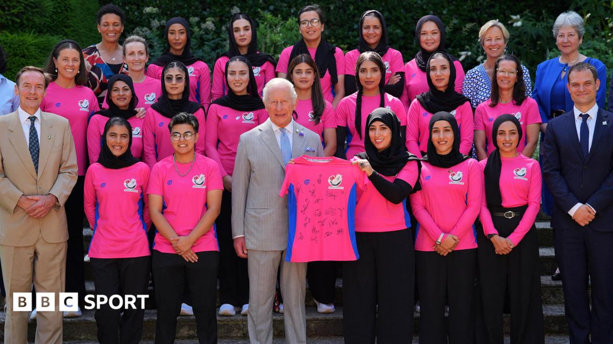 Members of the Afghanistan women's cricket team pose with King Charles, who is holding a signed shirt