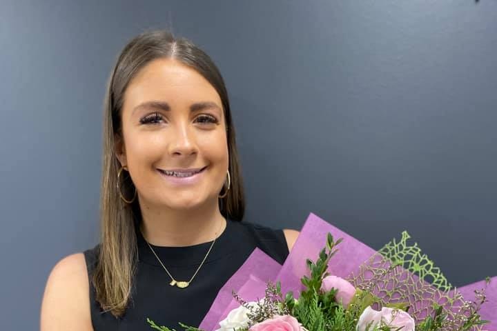 A smiling, dark-haired woman holds a bouquet of flowers.
