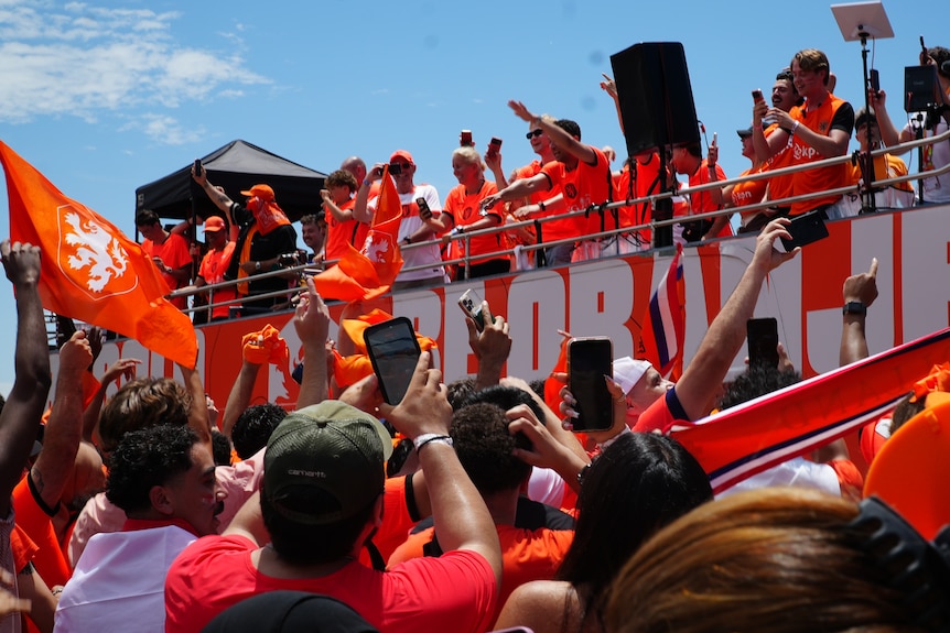 Fans clad in orange arrive at a stadium on an orange bus